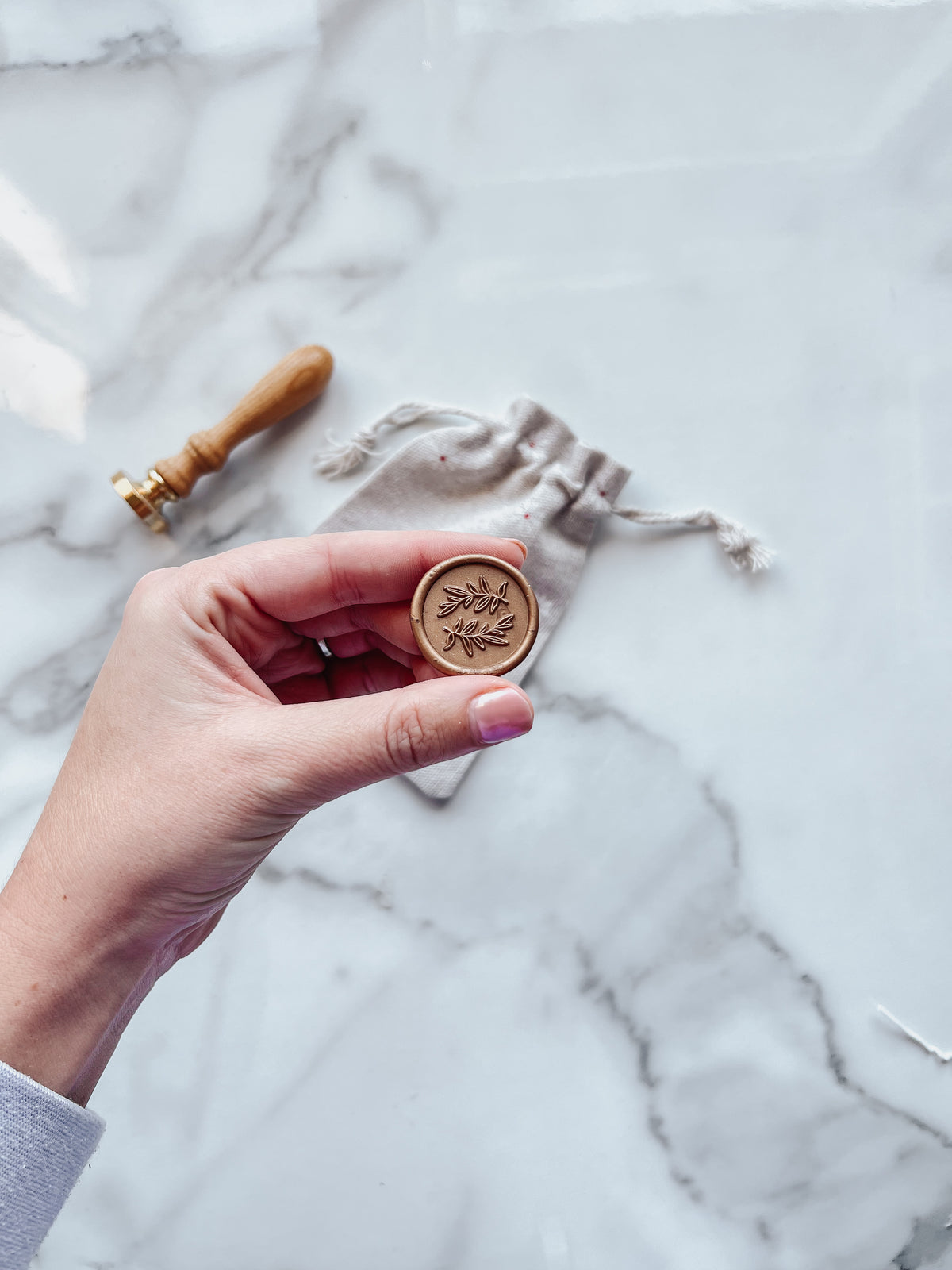 Hand holding a laurel wax seal with a marble background