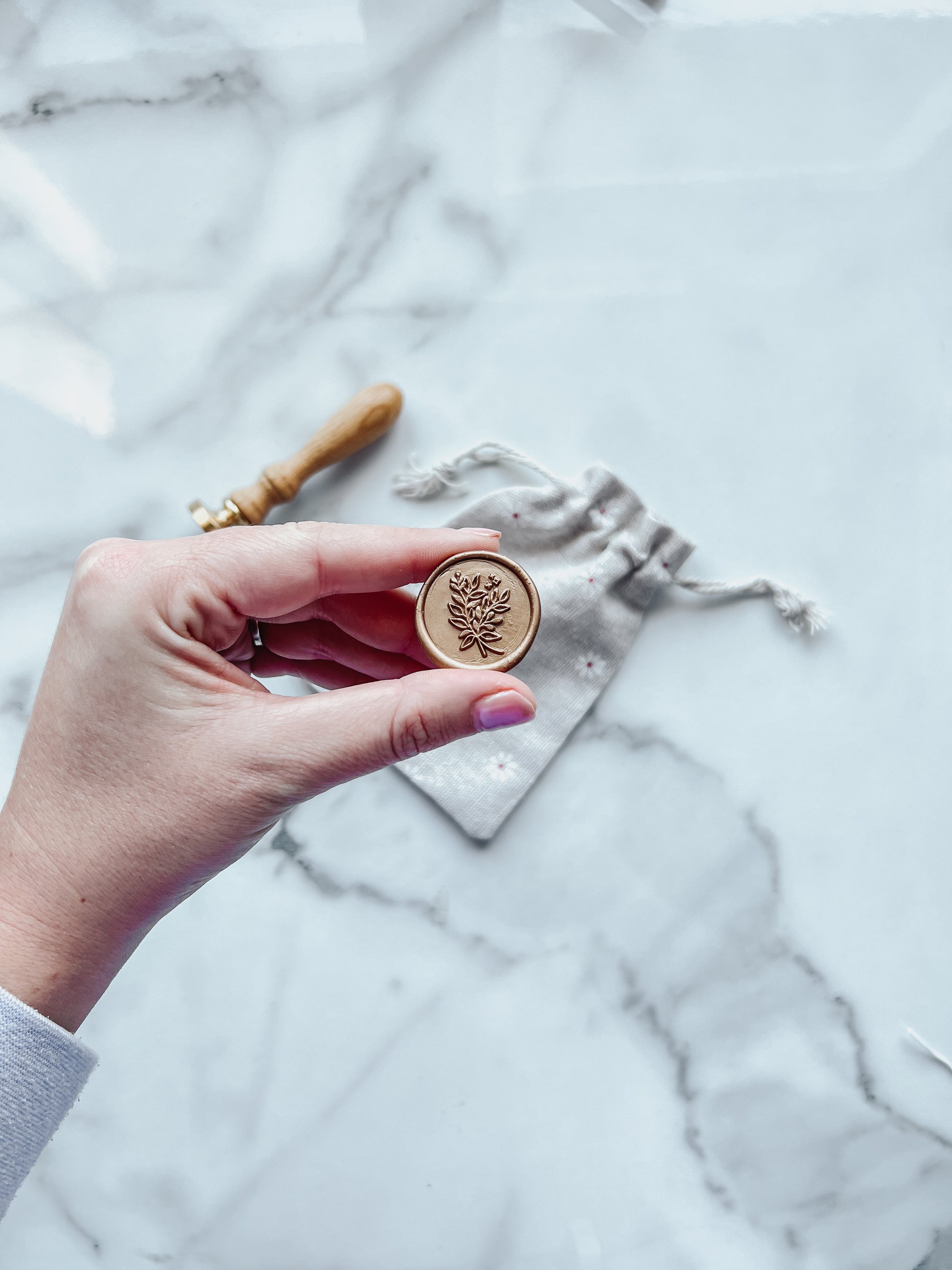 Hand holding a Wax Seal with a leafy design on a marble surface