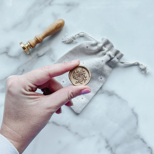 Hand holding a pretty floral wax seal on a marble surface.