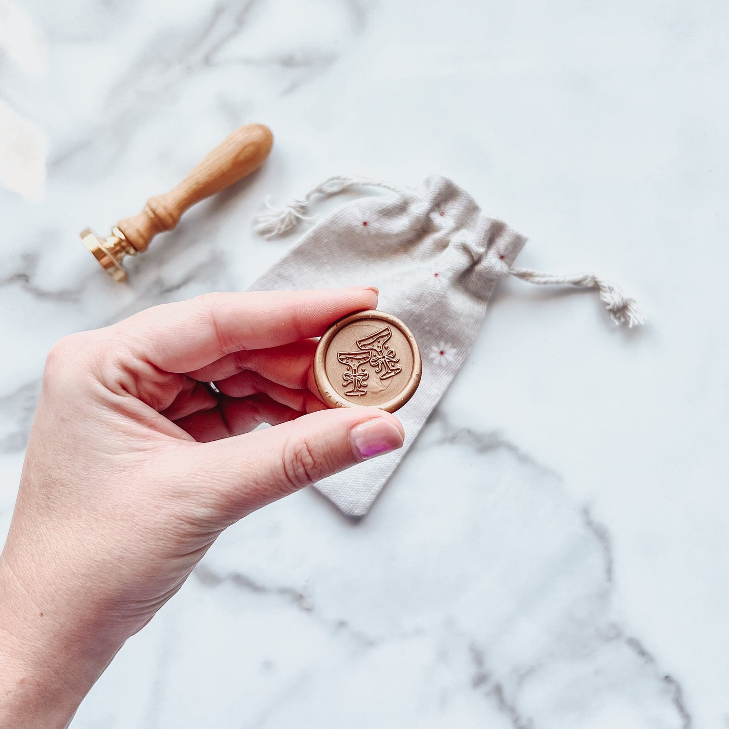 Hand holding a coupe glass wax seal with a marble background